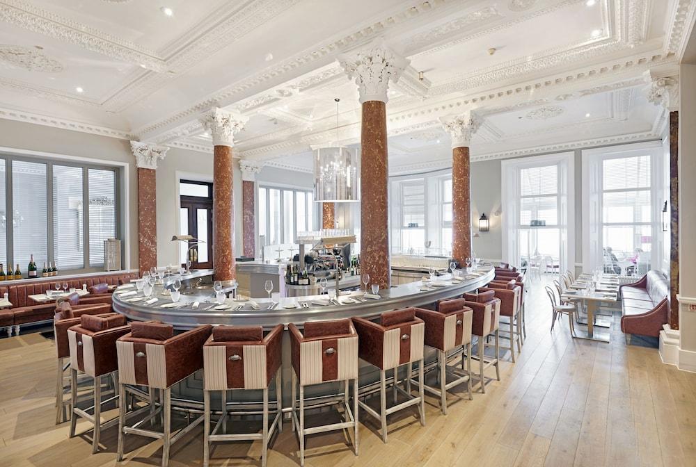 Hotel The Grand Hove Esterno foto The photo shows a stylish bar interior. It features a round bar counter with a polished metallic surface, surrounded by high stools with wooden and padded seats. The bar is accented by tall columns, which have a reddish-brown hue. The ceiling is ador