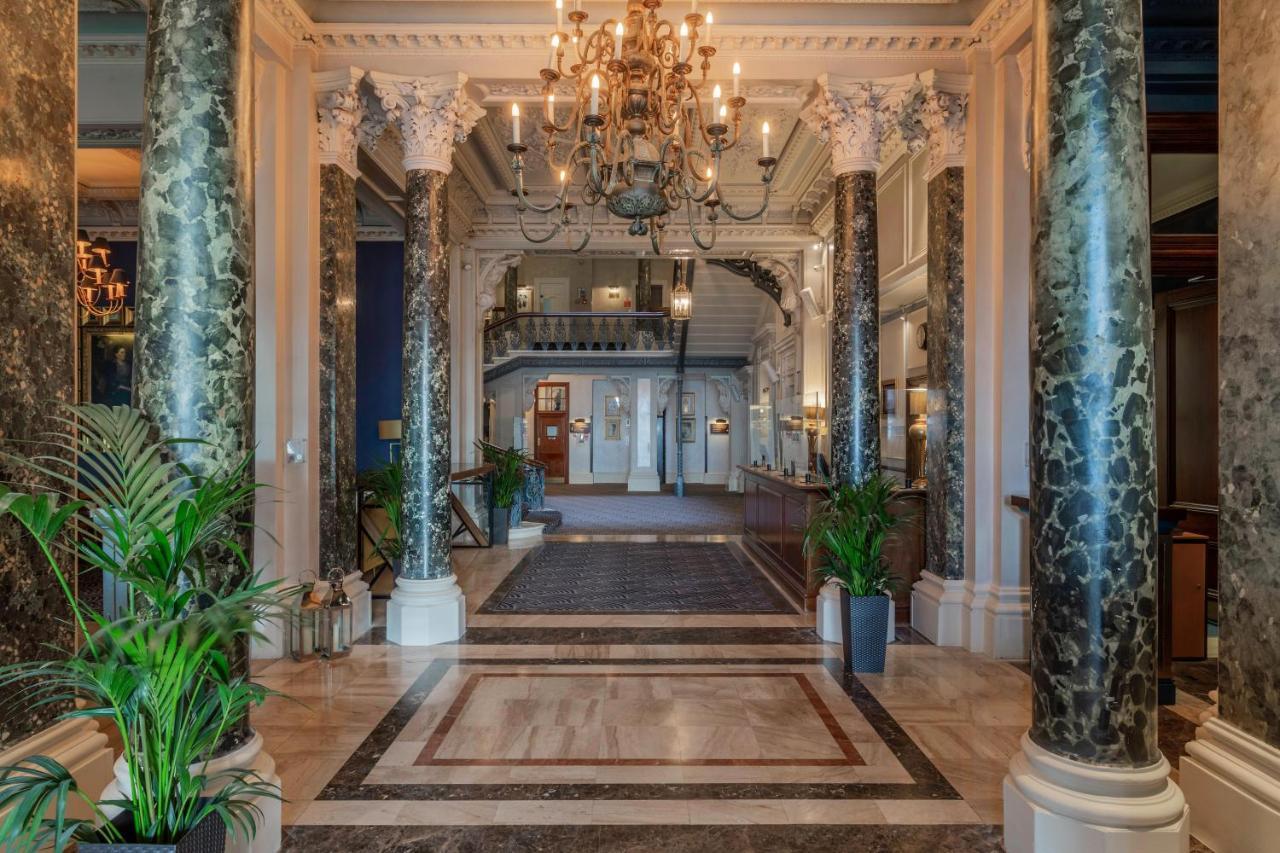 Hotel The Grand Hove Esterno foto The photo shows an elegant interior space, likely a hotel lobby or a grand entrance hall. The focal points include:

- **Decorative Columns**: Tall, ornate columns with a marble finish are visible, adding to the grandeur of the space.
- **Chandelier*