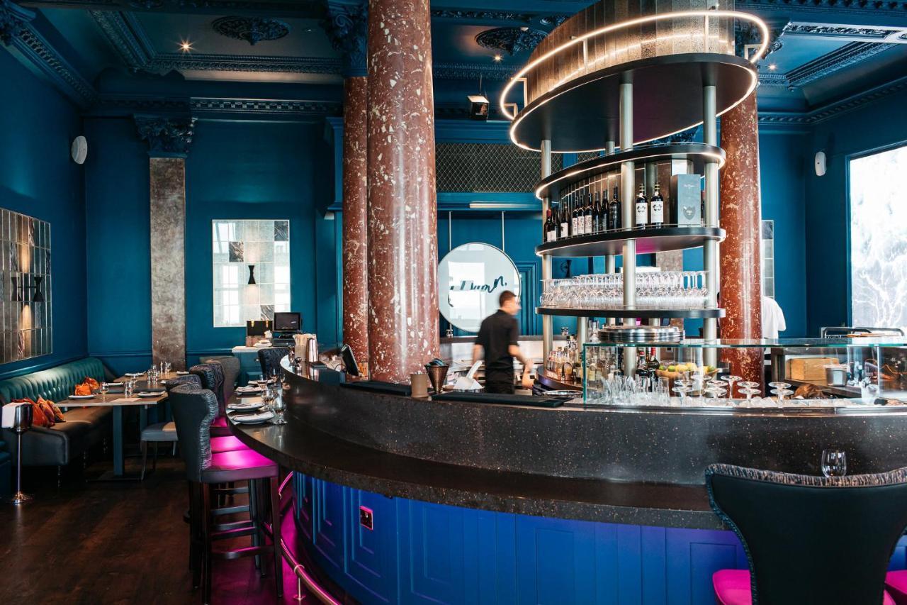 Hotel The Grand Hove Esterno foto The image depicts a stylish restaurant interior characterized by a vibrant blue color scheme. Prominent features include large, decorative pillars and a circular bar at the center, which is well-stocked with bottles. The seating areas have a modern d