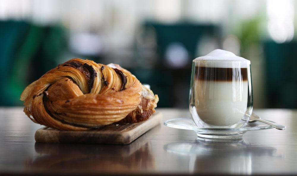 Hotel The Grand Hove Esterno foto The photo features a delicious pastry and a glass of coffee. The pastry, likely a sweet roll or pastry, has a golden-brown, flaky appearance and is arranged on a wooden board. Next to it, there is a clear glass of coffee layered with different shades