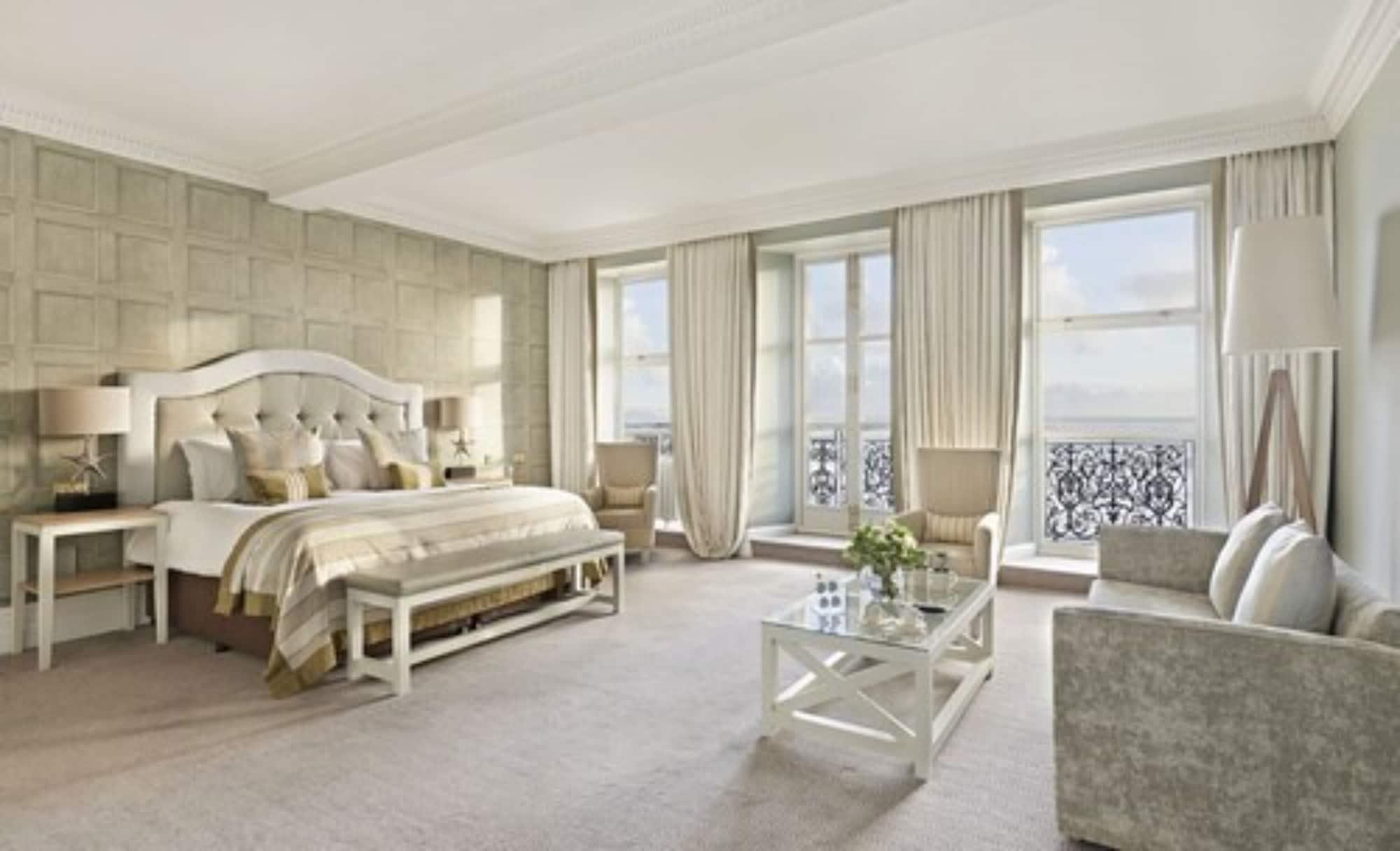 Hotel The Grand Hove Esterno foto The photo shows a spacious and elegantly decorated hotel room or suite. It features a large bed with a tufted headboard, adorned with plush pillows and a decorative bedspread. The room has light-colored walls, possibly with a textured pattern, and la