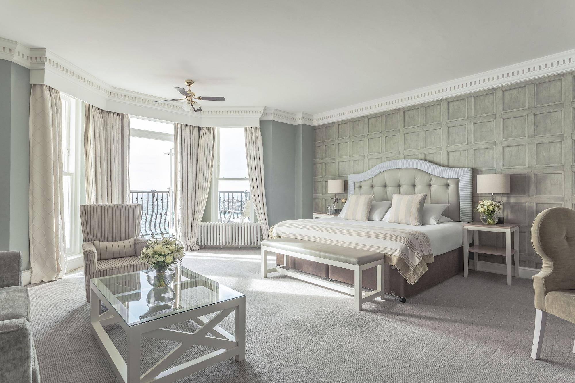 Hotel The Grand Hove Esterno foto The photo shows a spacious and elegantly designed hotel room. It features a large bed with light-colored bedding and a decorative headboard. On either side of the bed, there are small nightstands with lamps. There are two comfortable armchairs positi
