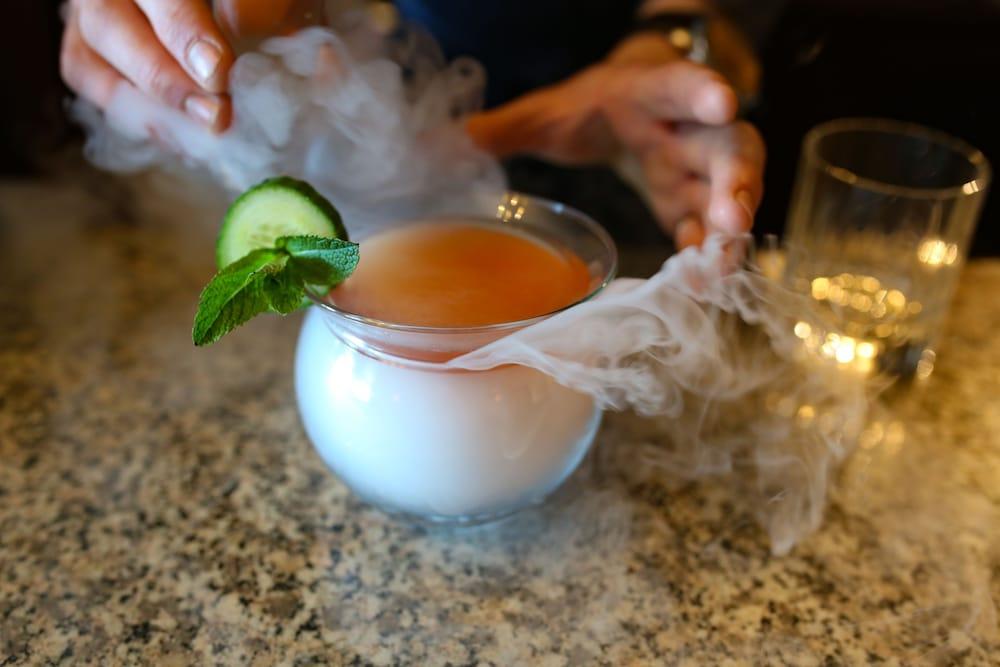 Hotel The Grand Hove Esterno foto The photo shows a cocktail in a round glass, with a layer of fog or steam around the top. The drink is garnished with a cucumber slice and a sprig of mint. One hand is reaching toward the glass, possibly to stir or serve the drink. The setting appear