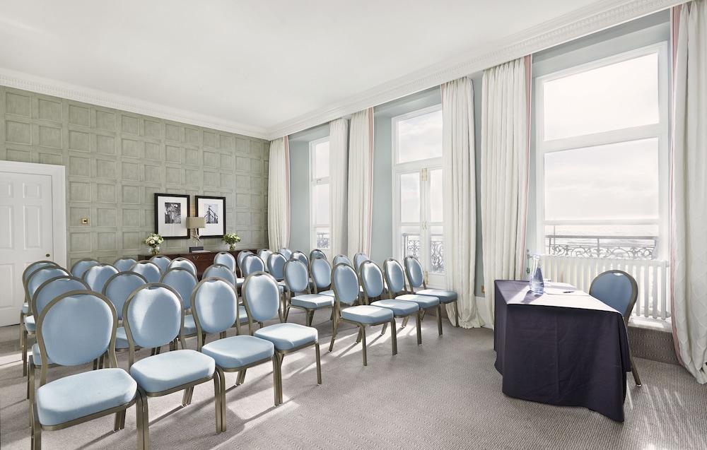 Hotel The Grand Hove Esterno foto The photo shows a well-lit meeting room with a modern and elegant design. There are several rows of blue chairs arranged neatly in front of a table covered with a dark cloth, likely intended for a speaker or presenter. The room features large windows