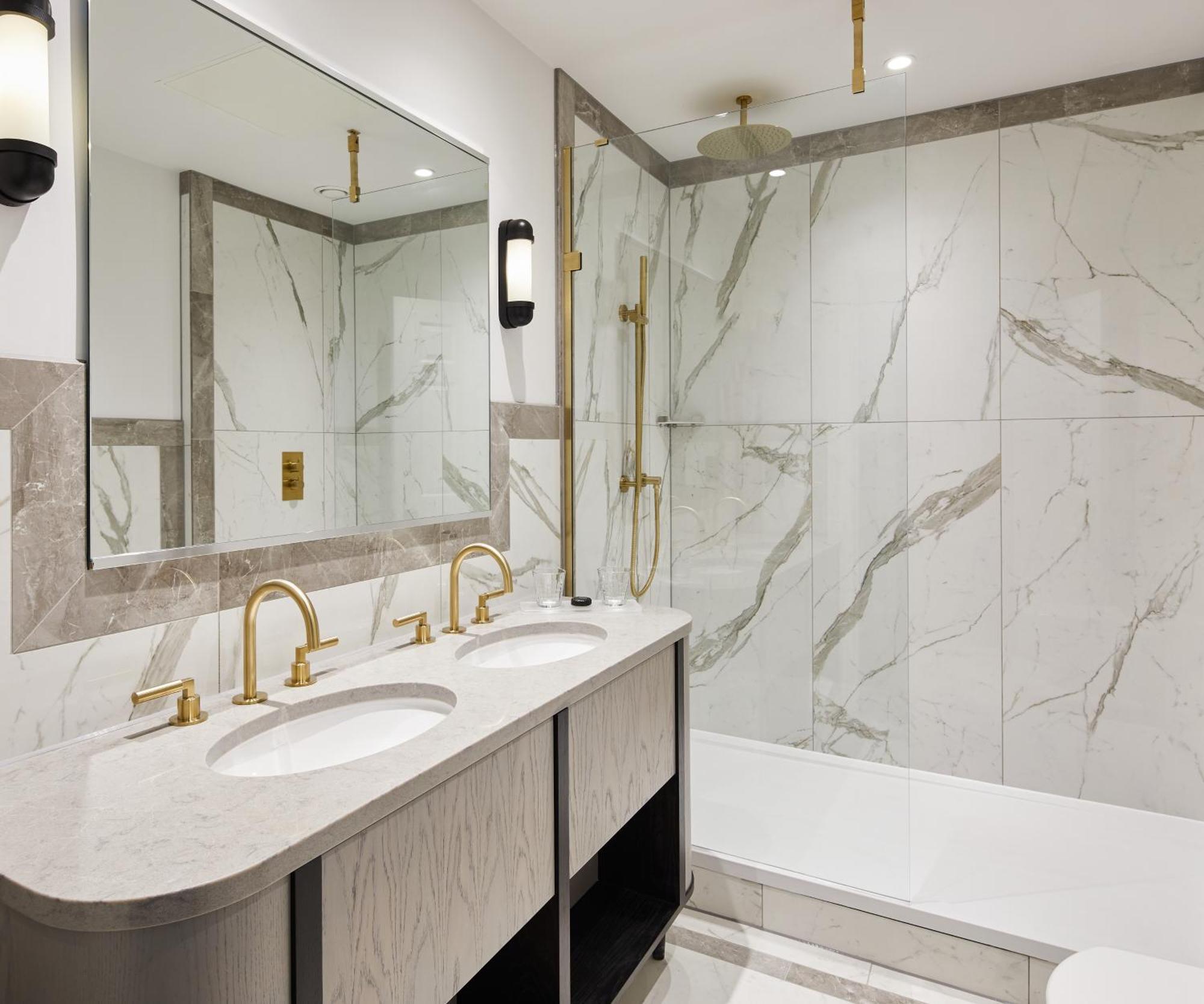 Hotel The Grand Hove Esterno foto The photo shows a modern bathroom featuring elegant design elements. It includes:

- A double vanity with two round sinks and stylish gold faucets.
- A large mirror above the vanity that reflects the space.
- A spacious shower area with marble tiling