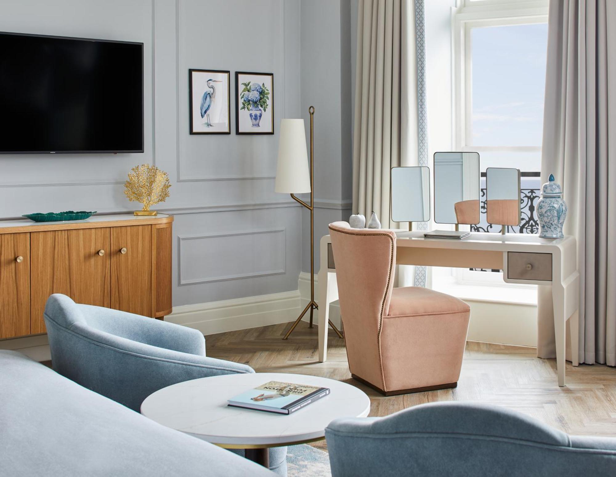 Hotel The Grand Hove Esterno foto The photo depicts an elegantly furnished room with a modern design. There is a television mounted on the wall opposite a light blue sofa. Nearby, a round coffee table holds a magazine or book. A wooden sideboard features decorative items, including a