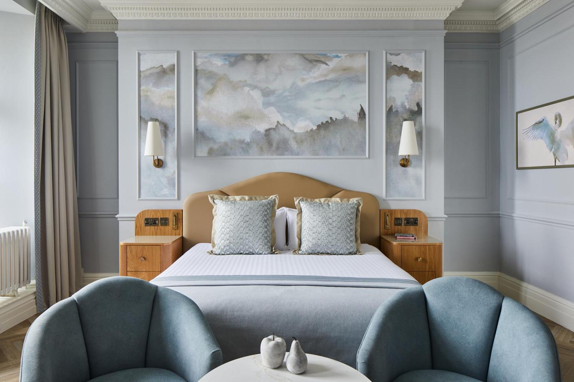 Hotel The Grand Hove Esterno foto The photo shows a beautifully designed hotel room. It features a large bed with a light-colored headboard and two decorative pillows on it. Behind the bed, there is a piece of artwork depicting soft, cloudy skies in pastel colors. On either side of t