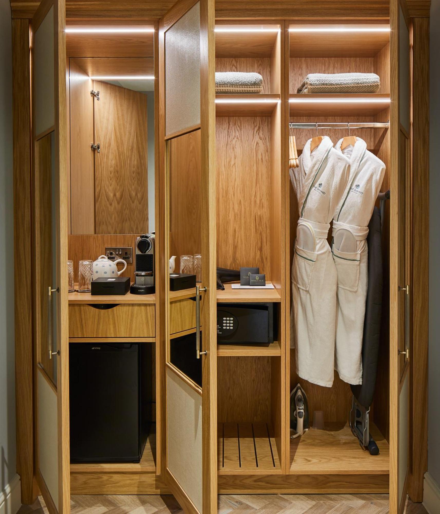 Hotel The Grand Hove Esterno foto The photo shows an elegantly designed closet or mini bar area featuring wooden cabinetry. Inside, there are two white bathrobes hanging on hangers, alongside various amenities. On the left side, there is a coffee maker along with mugs and other coffe