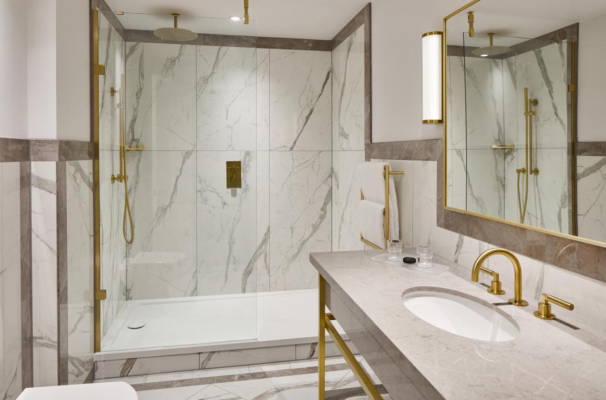 Hotel The Grand Hove Esterno foto The image shows a modern bathroom featuring a luxurious shower area and sink. The walls are covered in elegant marble tiles with a mix of light and dark tones. The shower has a glass enclosure and a sleek gold shower fixture. Next to the shower, ther