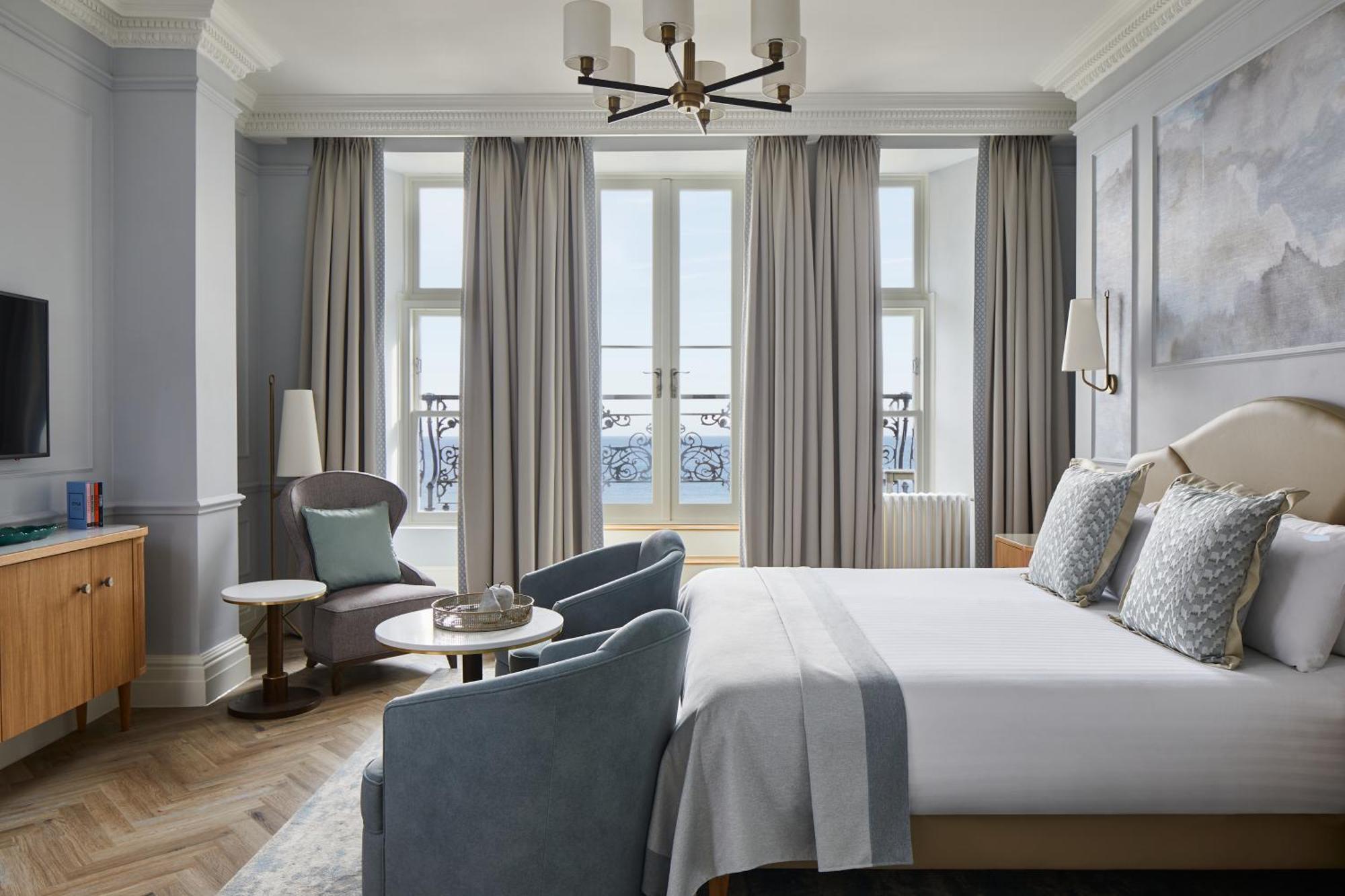 Hotel The Grand Hove Esterno foto The photo shows a modern hotel room designed with a stylish and sophisticated aesthetic. It features a large bed with soft linens and decorative pillows. On either side of the bed, there are bedside tables with lamps. A pair of comfortable chairs are
