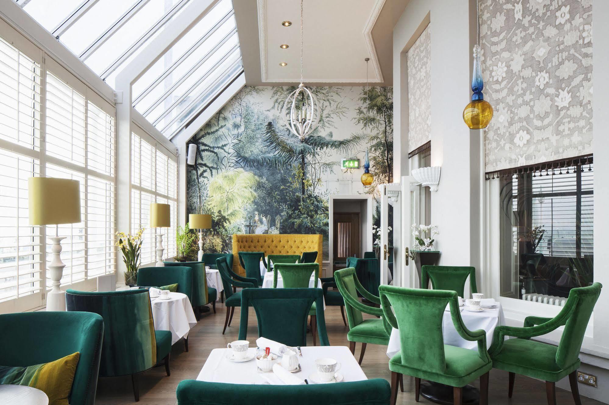 Hotel The Grand Hove Esterno foto The photo depicts a bright and elegant restaurant interior. The space features large windows that allow natural light to flood in, highlighting the greenery of the room. The walls are adorned with a nature-themed mural, creating a serene atmosphere. 