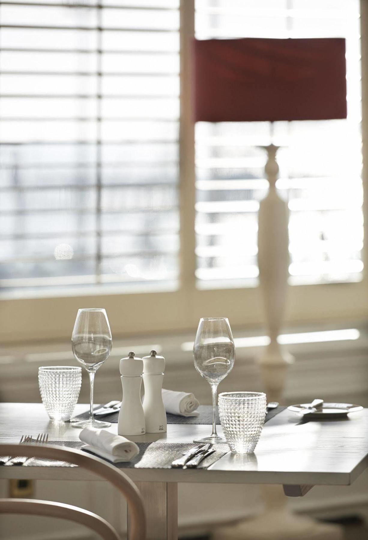 Hotel The Grand Hove Esterno foto The photo shows a dining table set for a meal. There are two wine glasses and a crystal glass positioned on the table. Additionally, there are salt and pepper shakers in the center, and a rolled napkin is also present. The background features large w