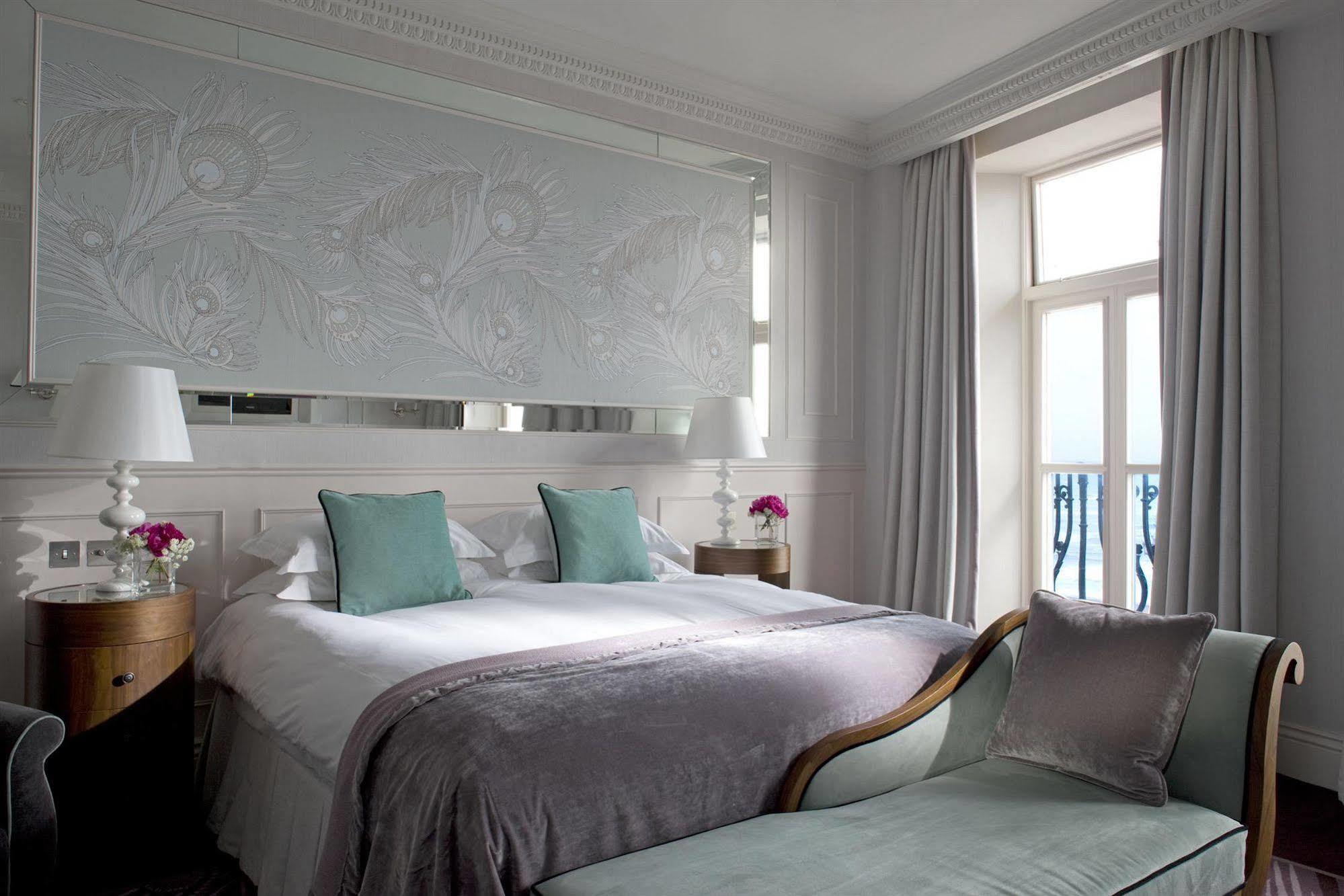 Hotel The Grand Hove Esterno foto The photo shows a modern and elegantly designed bedroom. It features a large bed with soft linens and two decorative pillows in a light teal color. The headboard is adorned with a subtle floral design, adding a touch of sophistication. Beside the bed