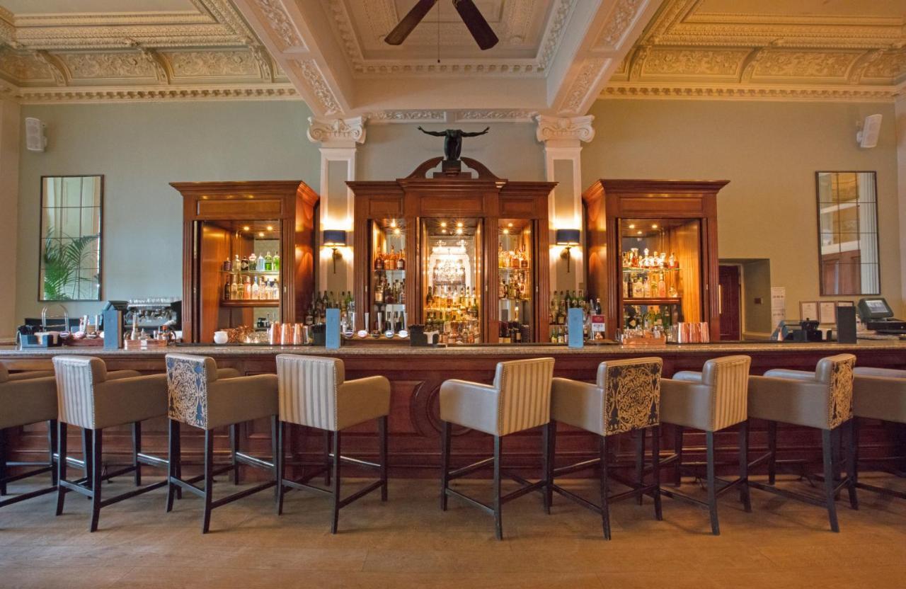 Hotel The Grand Hove Esterno foto The photo shows an elegant bar area within a sophisticated setting. The bar is made of rich wood and features a glass display with various bottles of alcohol visible inside. There are several high-backed bar stools arranged along the counter, which h