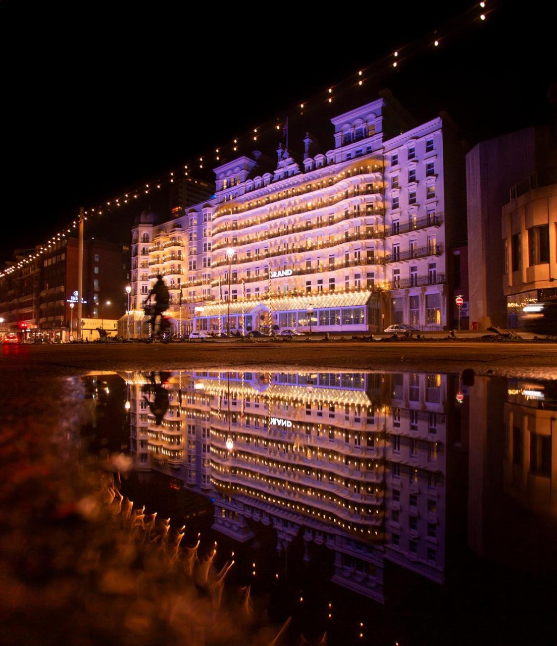 Hotel The Grand Hove Esterno foto The photo depicts a beautiful building illuminated at night, showcasing a mix of architectural details. The structure is adorned with lights that create a warm, inviting atmosphere, contributing to its vibrant appearance. In the foreground, there is 