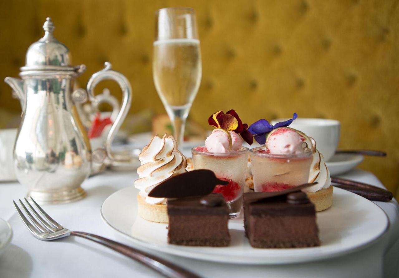 Hotel The Grand Hove Esterno foto The photo displays an elegant dessert presentation. On a white plate, there are two small pastries topped with meringue and garnished with colorful edible flowers, alongside a layer of fruit and possibly cream. There are also two rectangular pieces o