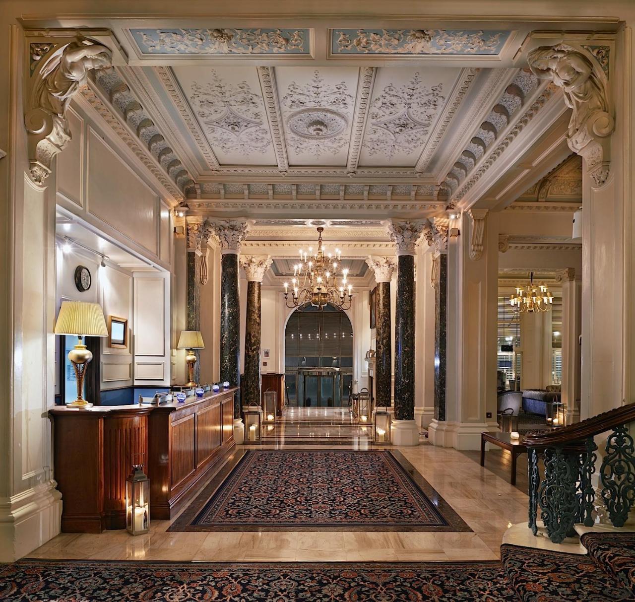 Hotel The Grand Hove Esterno foto The photo showcases an elegant hotel lobby. It features a reception desk made of dark wood, accented by soft lighting from lamps. The ceiling is intricately designed with decorative moldings, and a large chandelier hangs above, providing ambient ligh