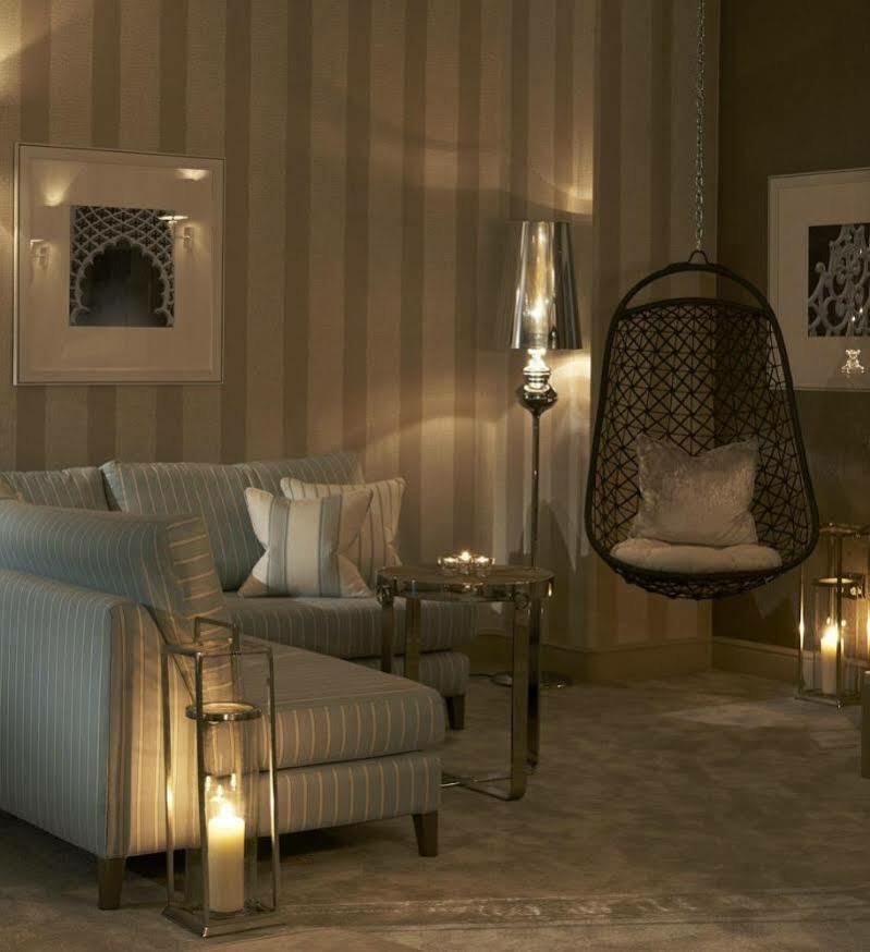 Hotel The Grand Hove Esterno foto The photo shows a stylish and modern living space. It features a cozy seating area with a light-colored striped sofa adorned with decorative pillows. Next to the sofa, there is a metallic side table, and a unique hanging chair made of wicker, providi